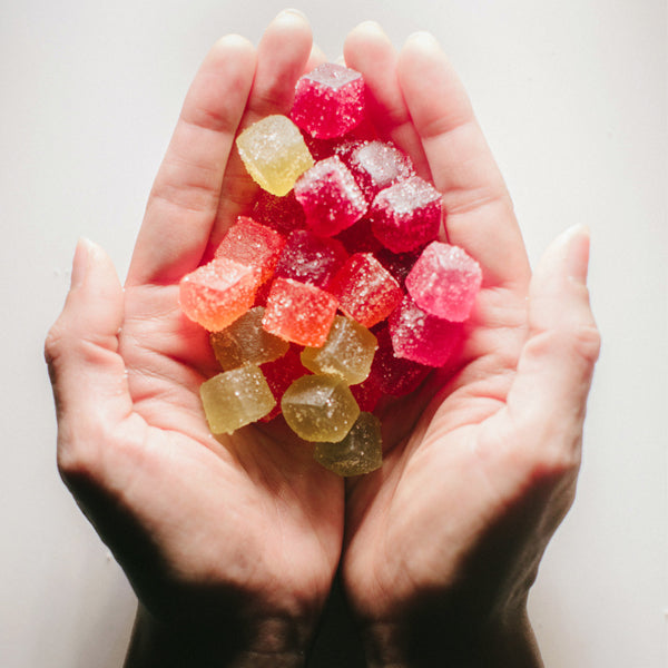 Hands holding an assortment of colorful, sugar-coated CBD gummies in various shapes and flavors, offering a tasty and convenient way to enjoy the benefits of CBD.